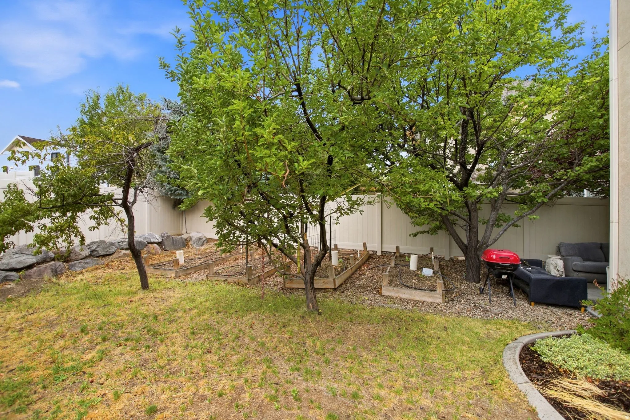 Private backyard oasis featuring mature shade trees, expansive lawn, and hardscaped planter beds