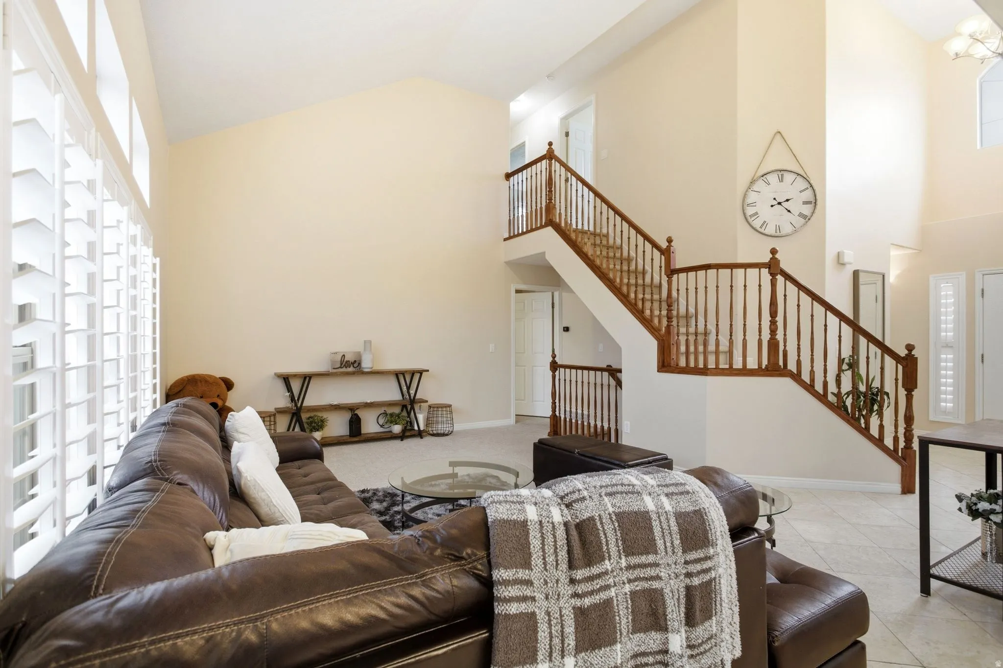 Open-concept living space featuring soaring vaulted ceilings, a two-story atrium with a floating staircase and wood-finish railings, large transom windows with plantation shutters providing natural light, and neutral paint finishes throughout