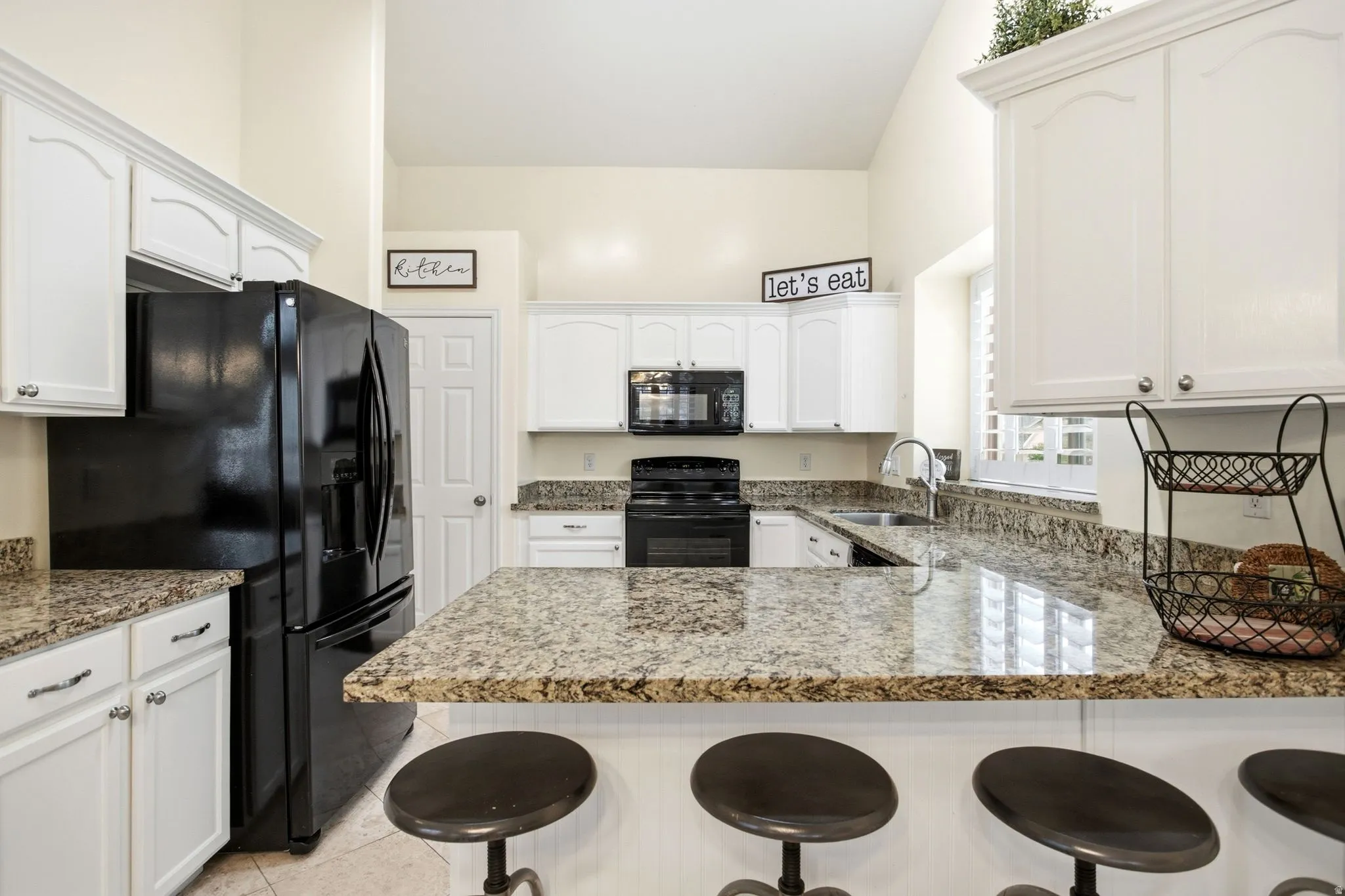Kitchen featuring white cabinetry, black appliances, granite countertops, tile flooring, and a vaulted ceiling