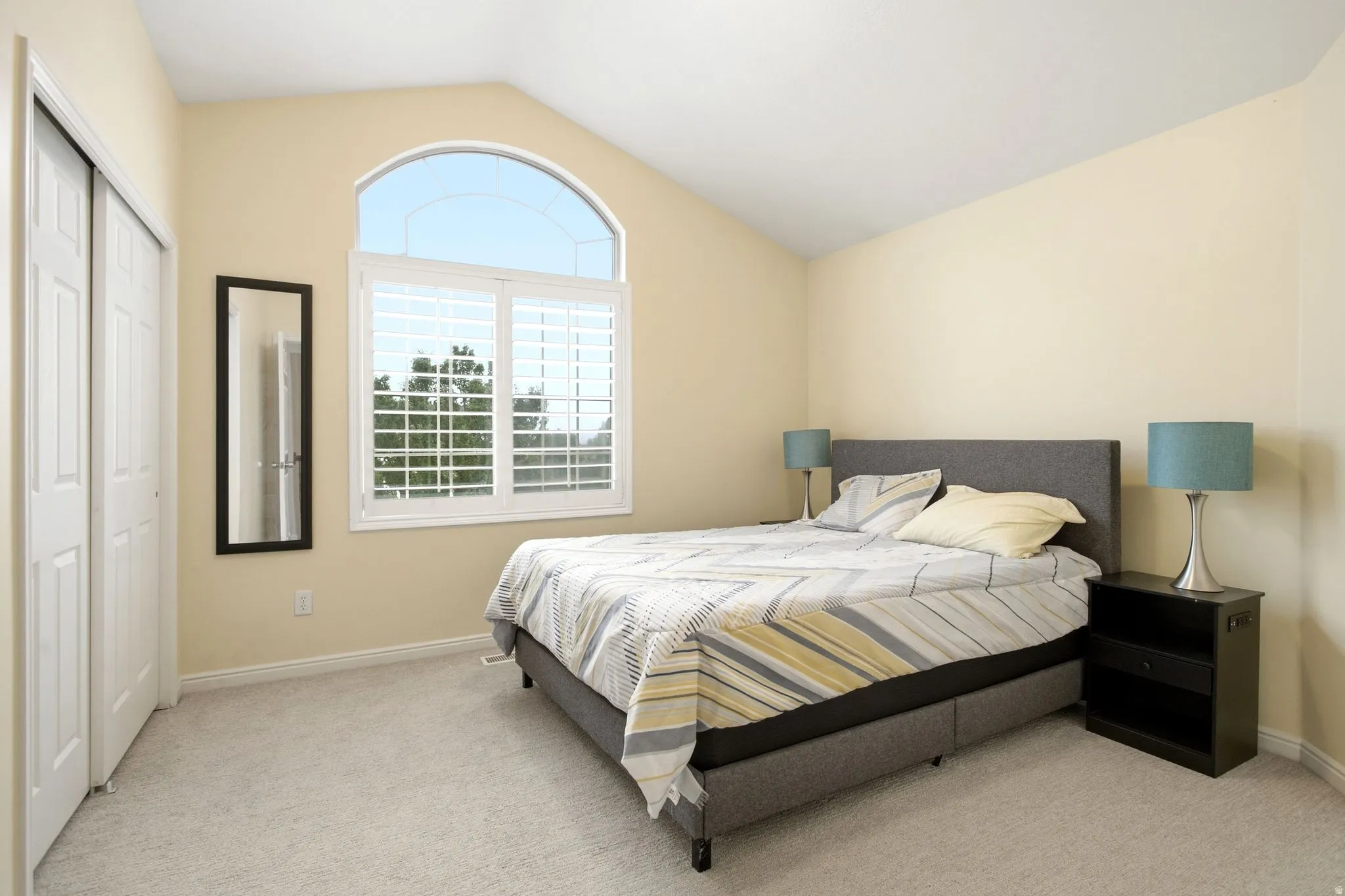 Vaulted ceiling with an arched window, white plantation shutters, light-toned carpeting, and bi-fold closet doors
