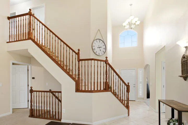 Two-story foyer featuring a grand staircase with wood railings, arched window, and tiled flooring