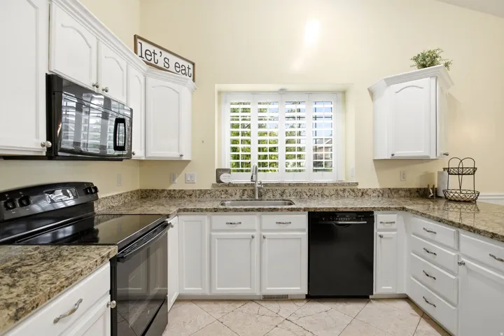 Bright, spacious kitchen featuring white cabinetry, granite countertops, black stainless steel appliances, and a center island with sink