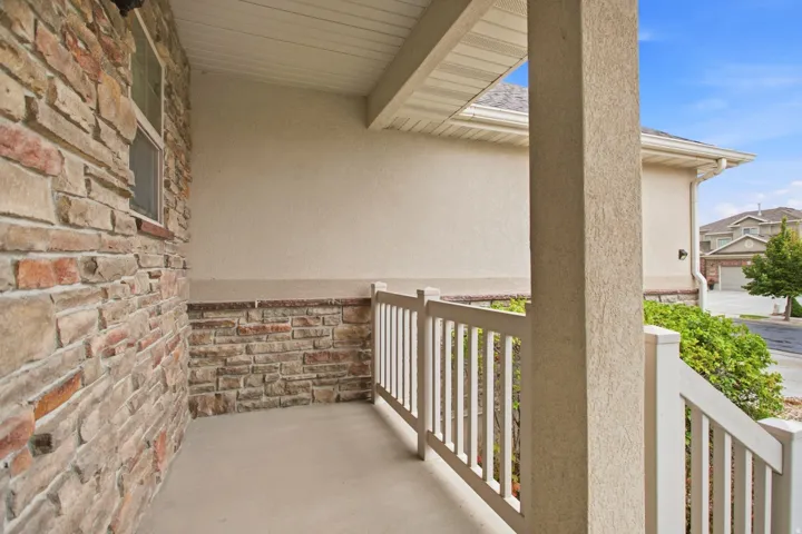 Covered porch with horizontal white railings, concrete flooring, and mixed-material exterior featuring exposed brick and stucco walls