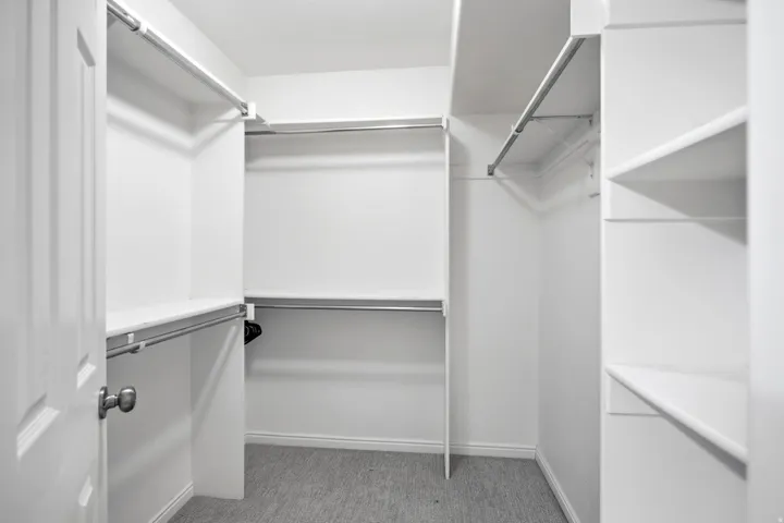 Spacious walk-in closet featuring double hanging rods, multiple shelving units, and abundant storage capacity with neutral finishes and clean lines throughout