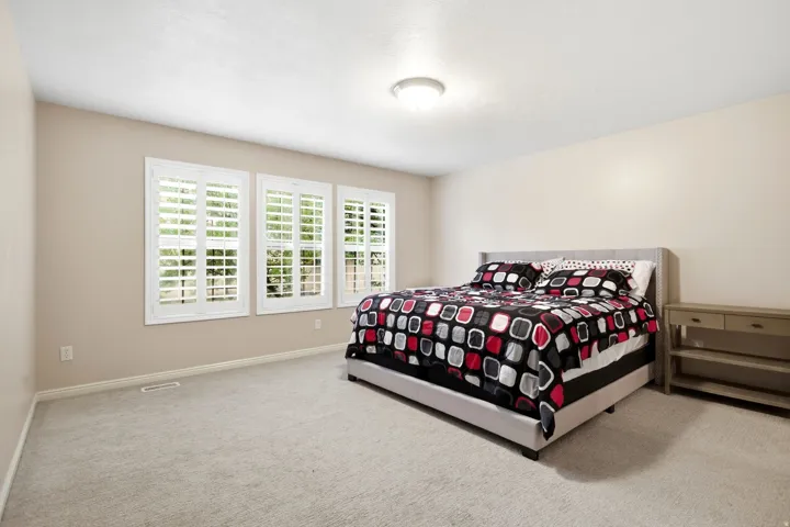 Spacious secondary bedroom featuring neutral wall finishes, plush carpeting, and abundant natural light from three plantation shutter-adorned windows