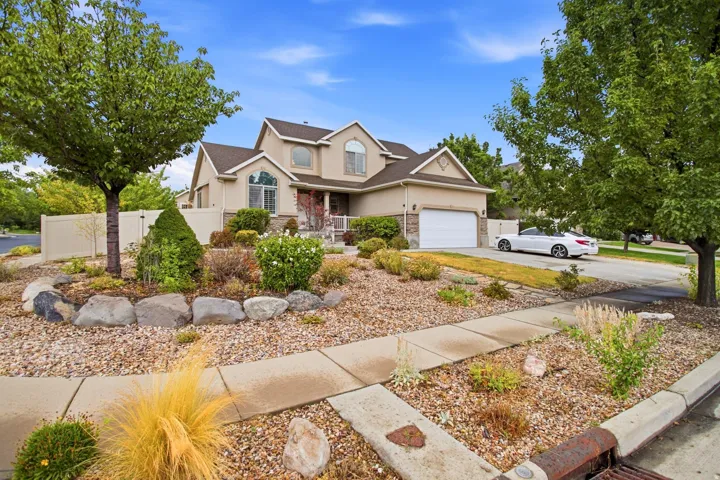 Two-story residence featuring a two-car garage, professional landscaping with mature trees, decorative rock and stone hardscaping, manicured lawn, and a concrete driveway approach