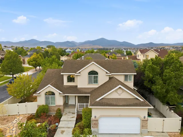 Stucco exterior with stone accents, attached garage, concrete driveway, and mature landscaping