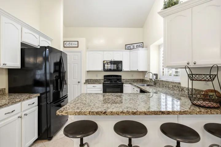 Kitchen featuring white cabinetry, black appliances, granite countertops, tile flooring, and a vaulted ceiling