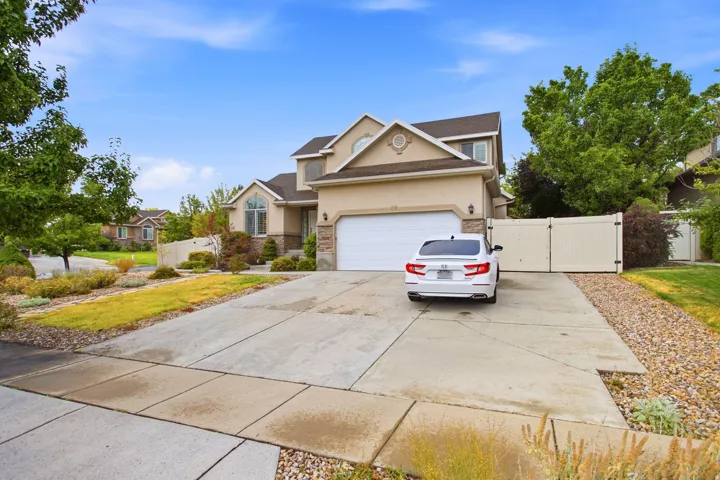 Welcoming two-story residence showcasing a wide concrete driveway with integrated parking, white garage door, and manicured front landscaping with mature trees and drought-resistant plantings
