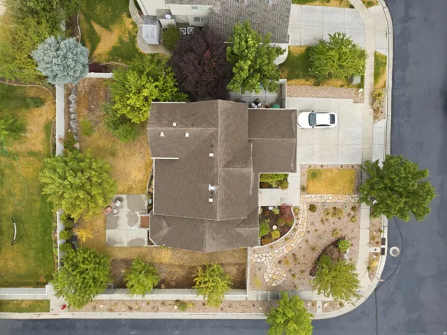 Aerial view showcasing a contemporary residence with a dark composite roof, concrete driveway with parking space, and professionally landscaped grounds featuring mature trees and manicured lawn areas