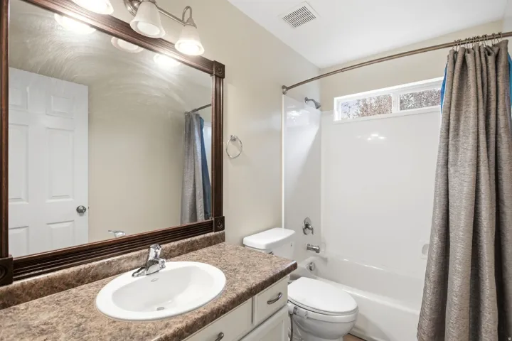 Spa-inspired bathroom featuring a granite-topped vanity with an undermount sink, framed mirror with integrated lighting, and a combined shower-tub enclosure with tile surround and coordinating neutral curtain