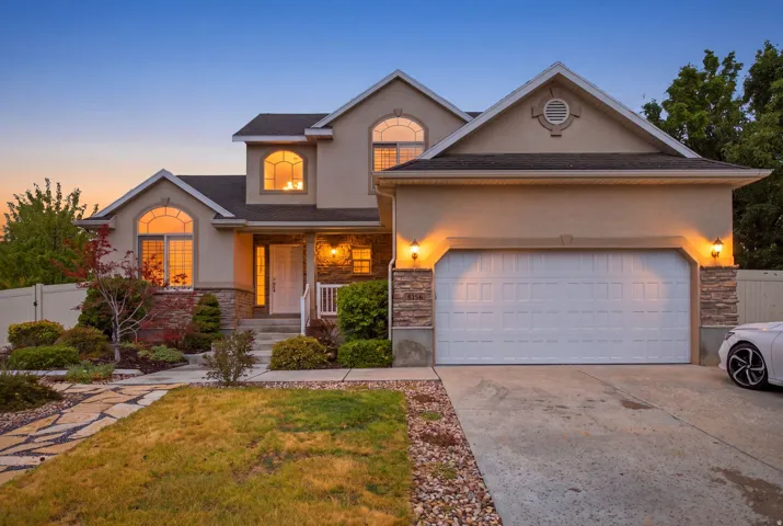 Stucco exterior with stone accents, arched windows, an attached garage, landscaped front yard, and a stone-paver walkway
