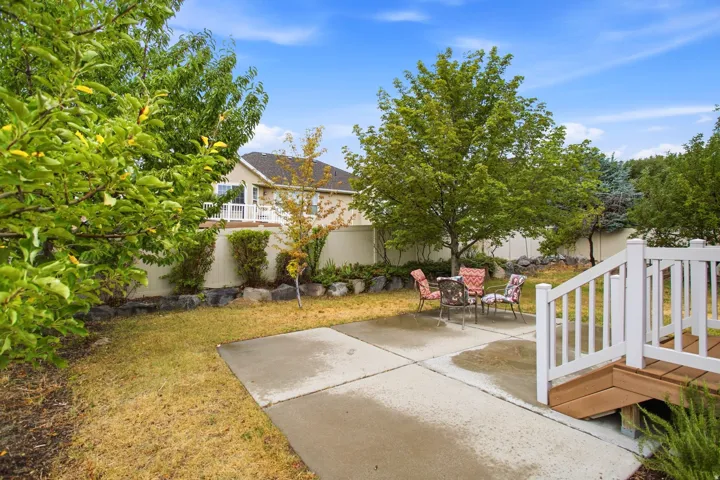 Expansive backyard featuring a concrete patio, wood-finish deck with white railings, mature trees, and a privacy fence