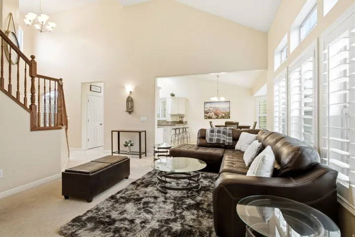 Spacious great room showcasing vaulted ceilings, abundant natural light from multiple windows with plantation shutters, and a wood-finish flooring throughout