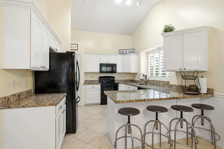 Spacious kitchen featuring white cabinetry, granite countertops, black appliances, tile flooring, and a large island with seating for multiple guests