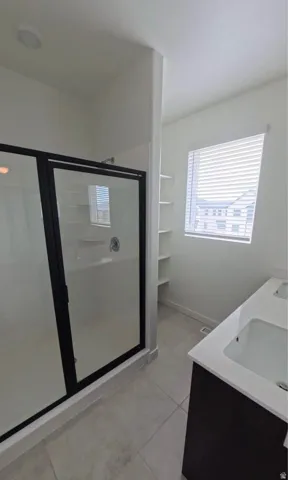 Enclosed shower with black-framed glass, dual vanity with undermount sinks, built-in shelving, and tile flooring