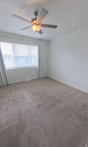 Neutral-toned carpeting, window with horizontal blinds, and a ceiling fan with integrated lighting