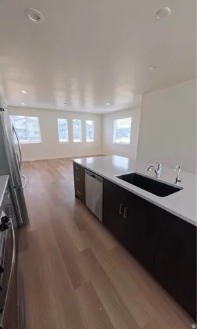 Open-concept living space with wood-finish flooring, a kitchen island with integrated sink, stainless steel appliances, and recessed lighting