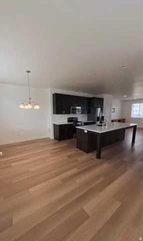Wood-finish flooring throughout, dark wood-finish cabinetry, stainless steel appliances, large kitchen island with integrated sink, and recessed lighting
