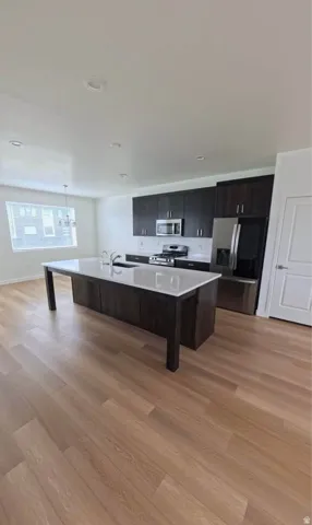 Modern kitchen featuring dark wood-finish cabinetry, stainless steel appliances, a center island with white countertops, and wood-finish flooring
