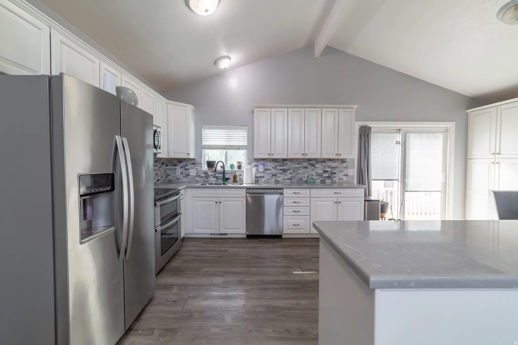 Kitchen featuring white cabinetry, stainless steel appliances, a tile backsplash, wood-finish flooring, and a vaulted ceiling