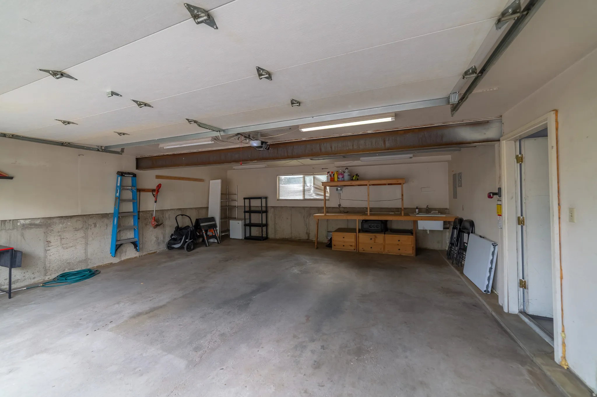 Concrete flooring, fluorescent lighting, exposed structural beam, built-in shelving, and utility sink
