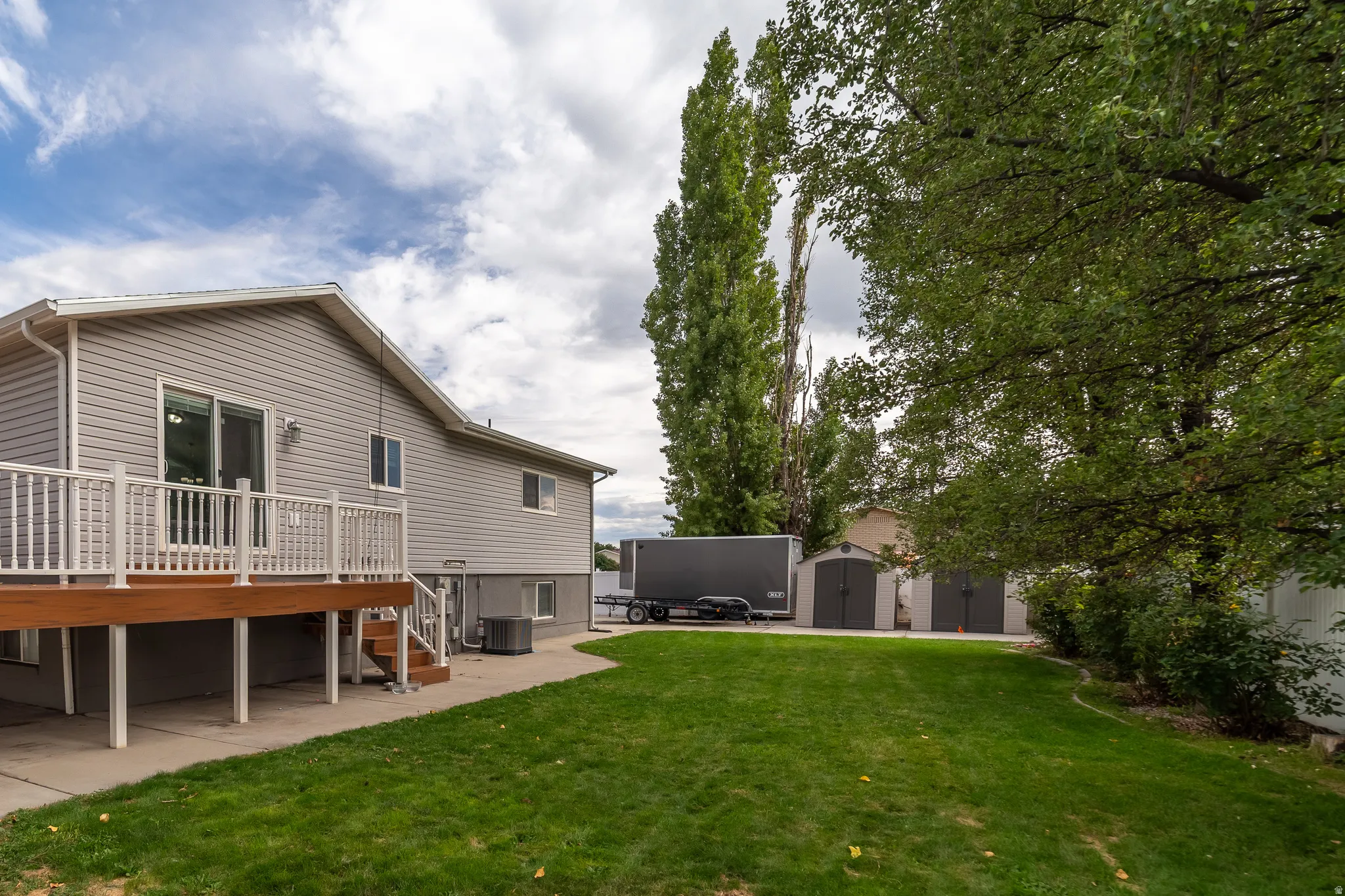 Expansive green lawn, two detached storage sheds, and mature perimeter trees