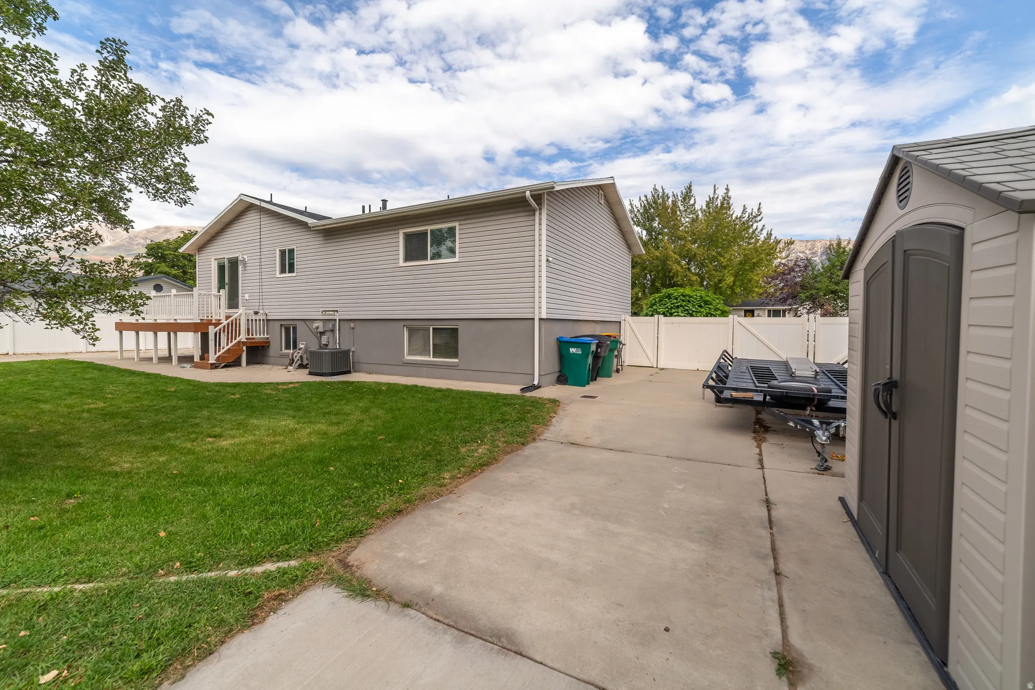 Expansive backyard featuring a manicured lawn, concrete patio, and a wood-decked porch with railing