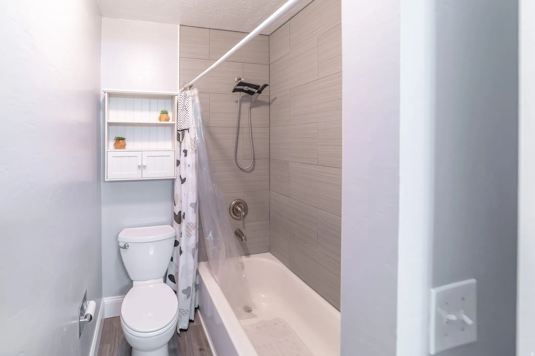 Bathtub with tiled surround, white toilet, and wood-finish flooring