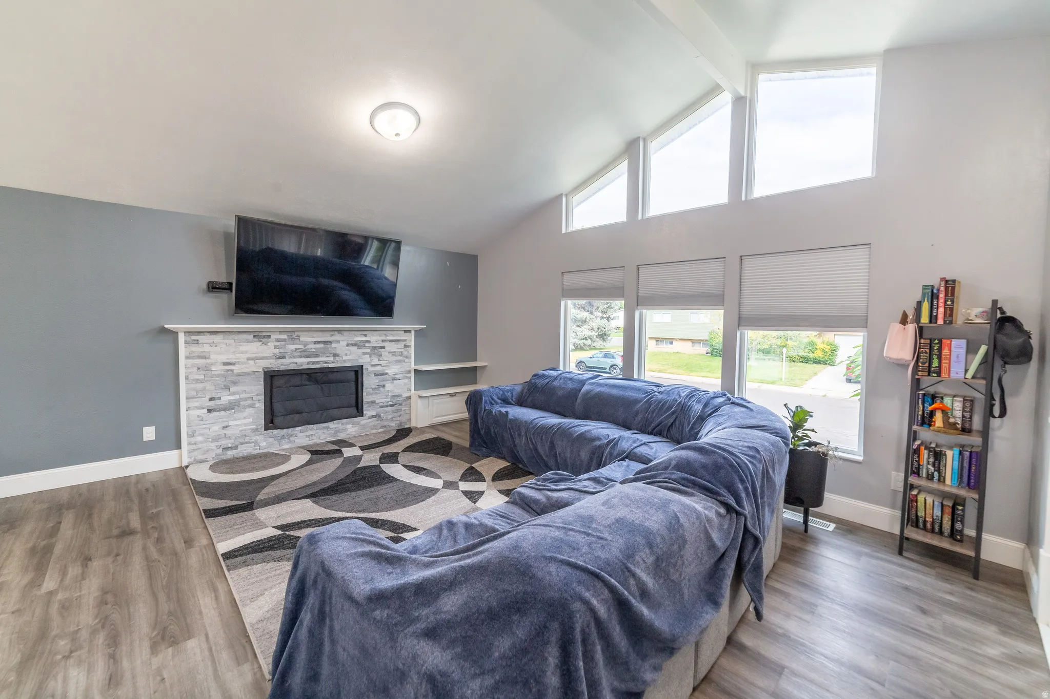 Vaulted ceiling, stone-clad fireplace with mantel, recessed fireplace insert, wood-finish flooring, and multiple windows