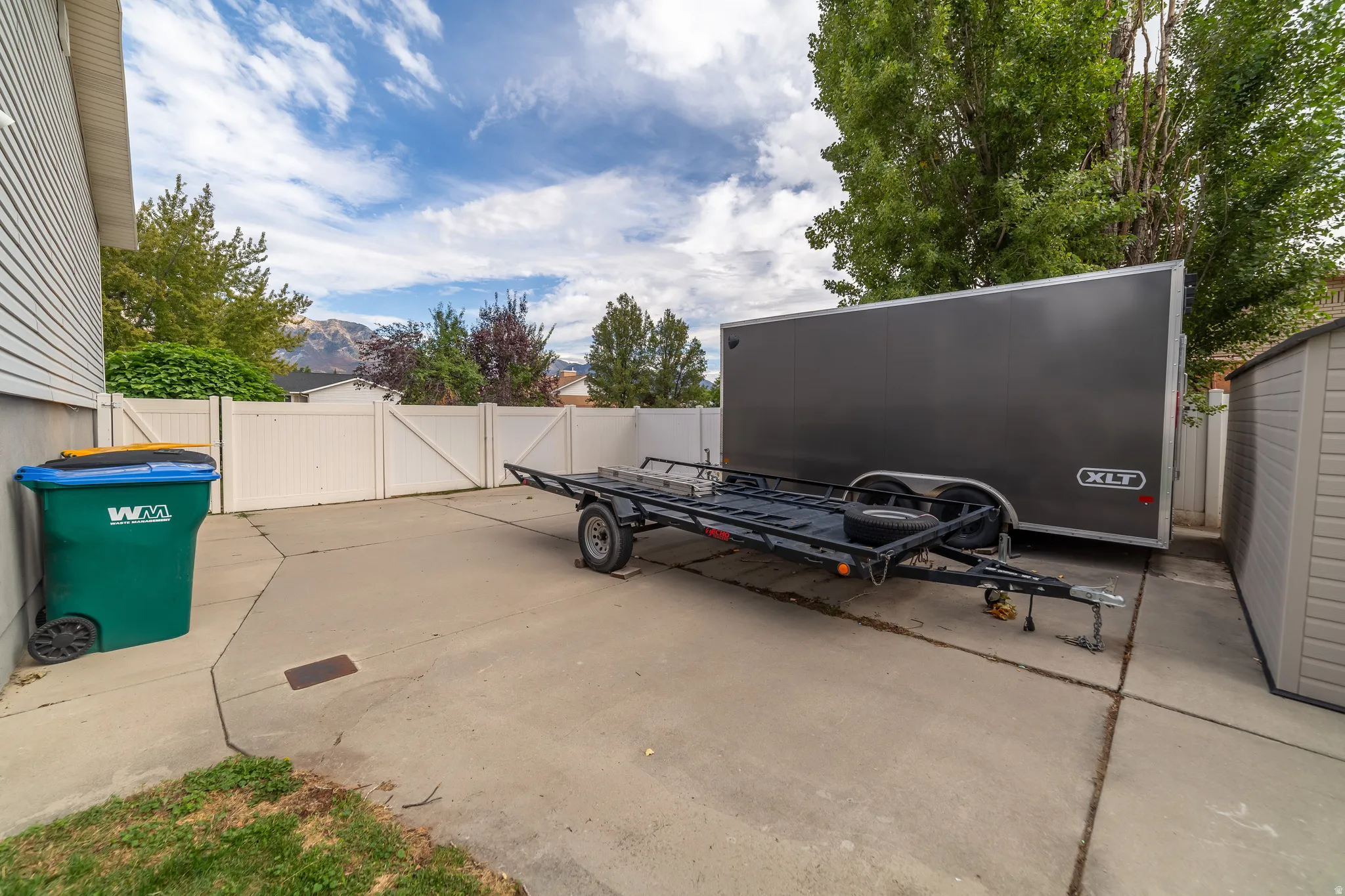 Paved side yard with white vinyl fencing and a plastic storage shed