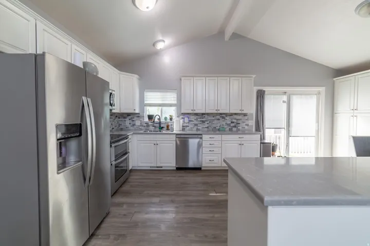Kitchen featuring white cabinetry, stainless steel appliances, a tile backsplash, wood-finish flooring, and a vaulted ceiling
