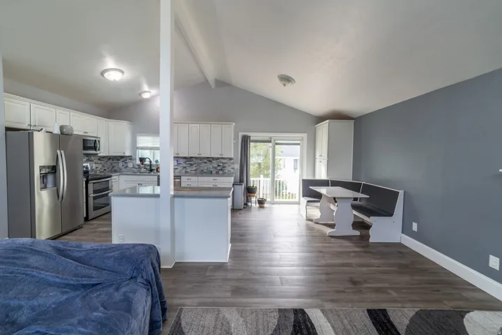 Vaulted ceiling, wood-finish flooring, kitchen with white cabinetry, stainless steel appliances, and a tiled backsplash, and a sliding glass door