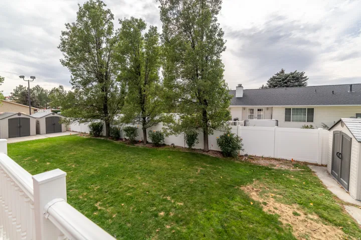 Expansive yard with green lawn, mature trees, white privacy fencing, and two storage sheds