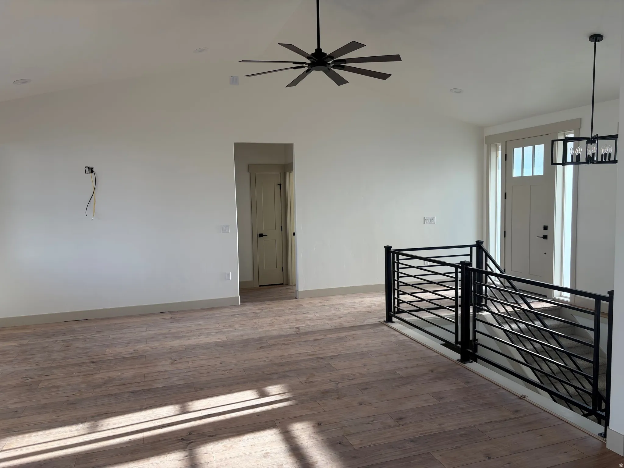 Vaulted ceiling with a contemporary ceiling fan, wood-finish flooring, and sleek metal stair railing