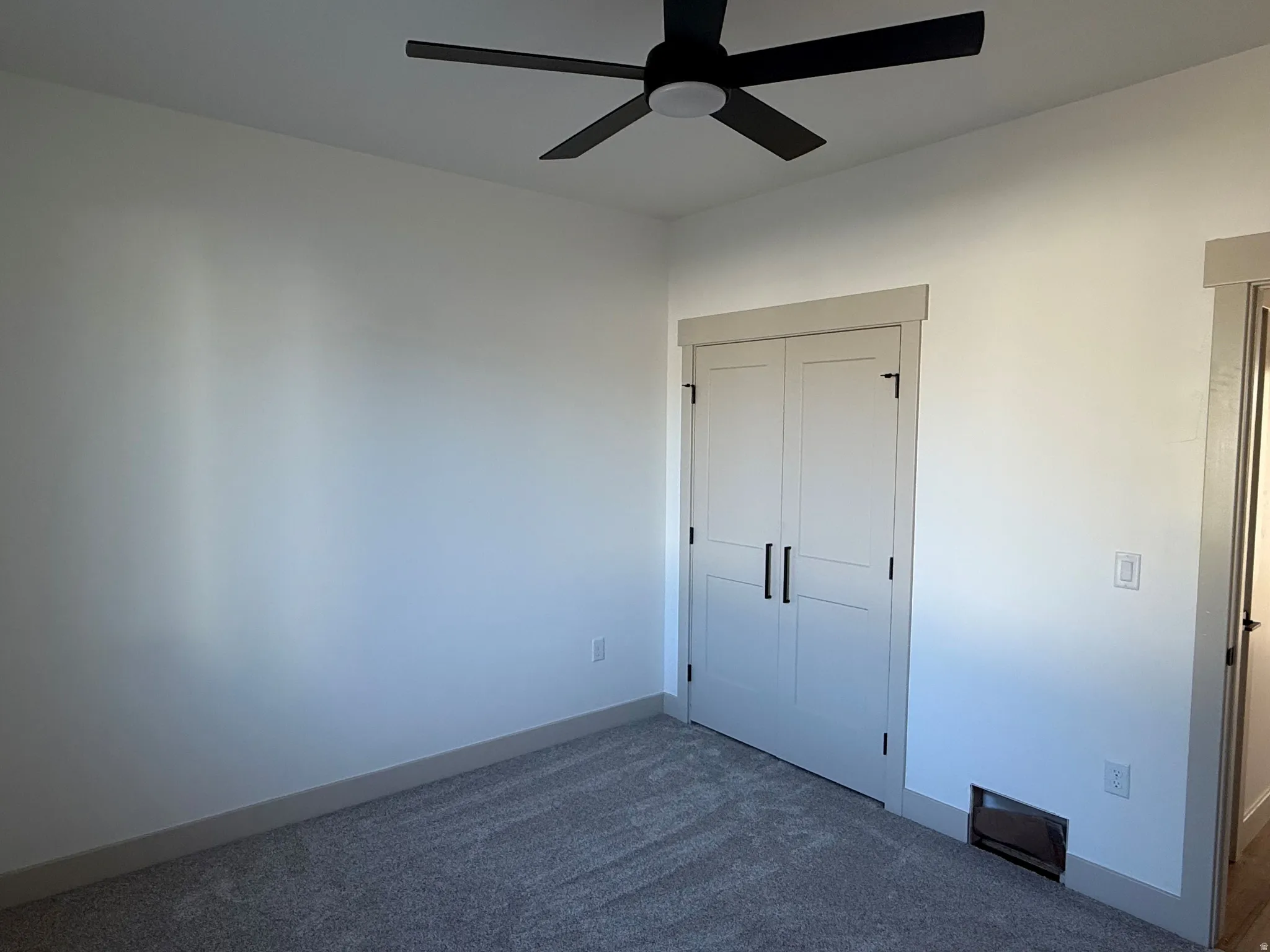 White walls and gray carpeting with a black ceiling fan, white bifold closet doors, and light gray trim