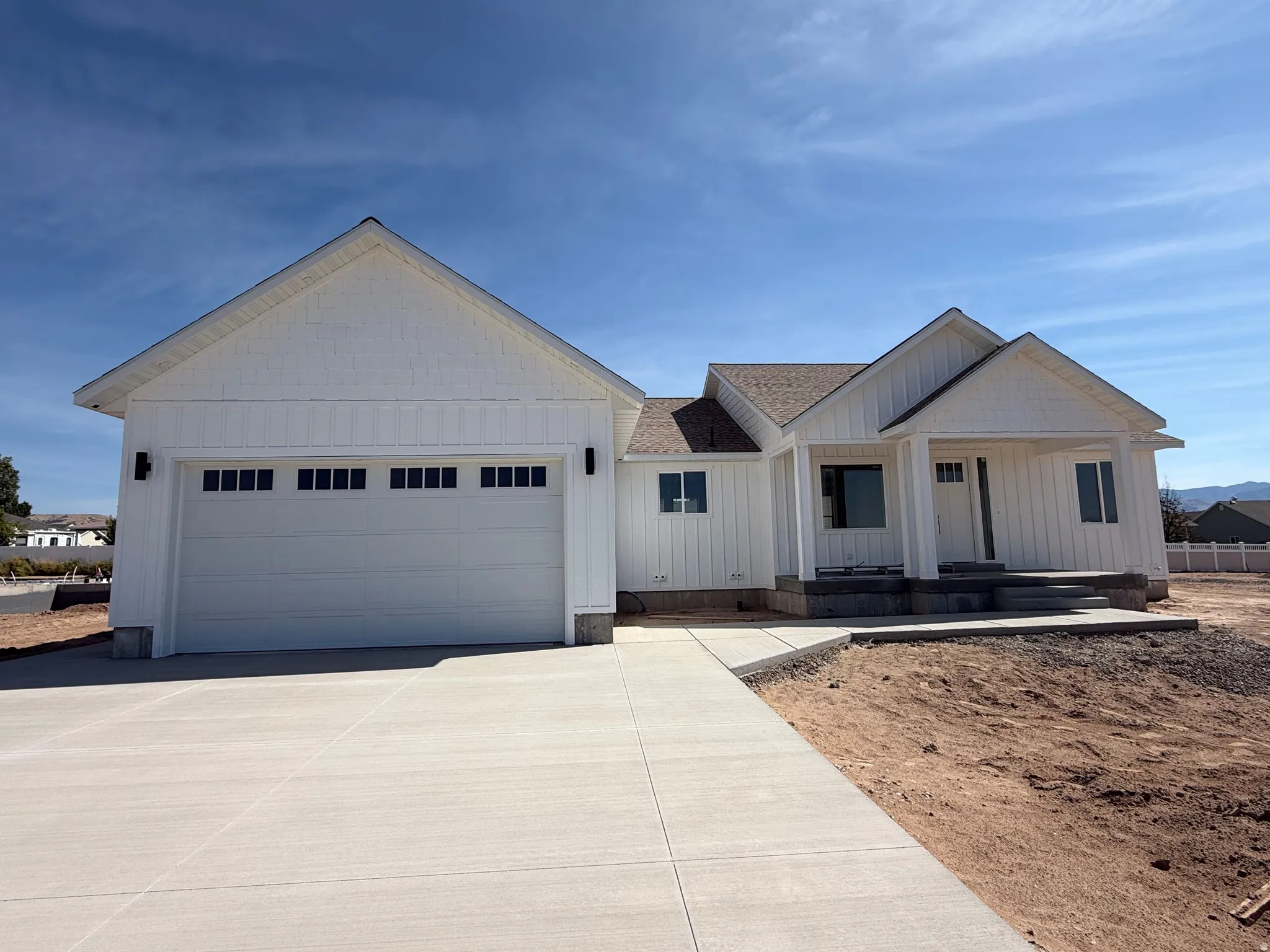 Contemporary exterior featuring white board and batten siding, attached garage, covered front porch, and concrete driveway