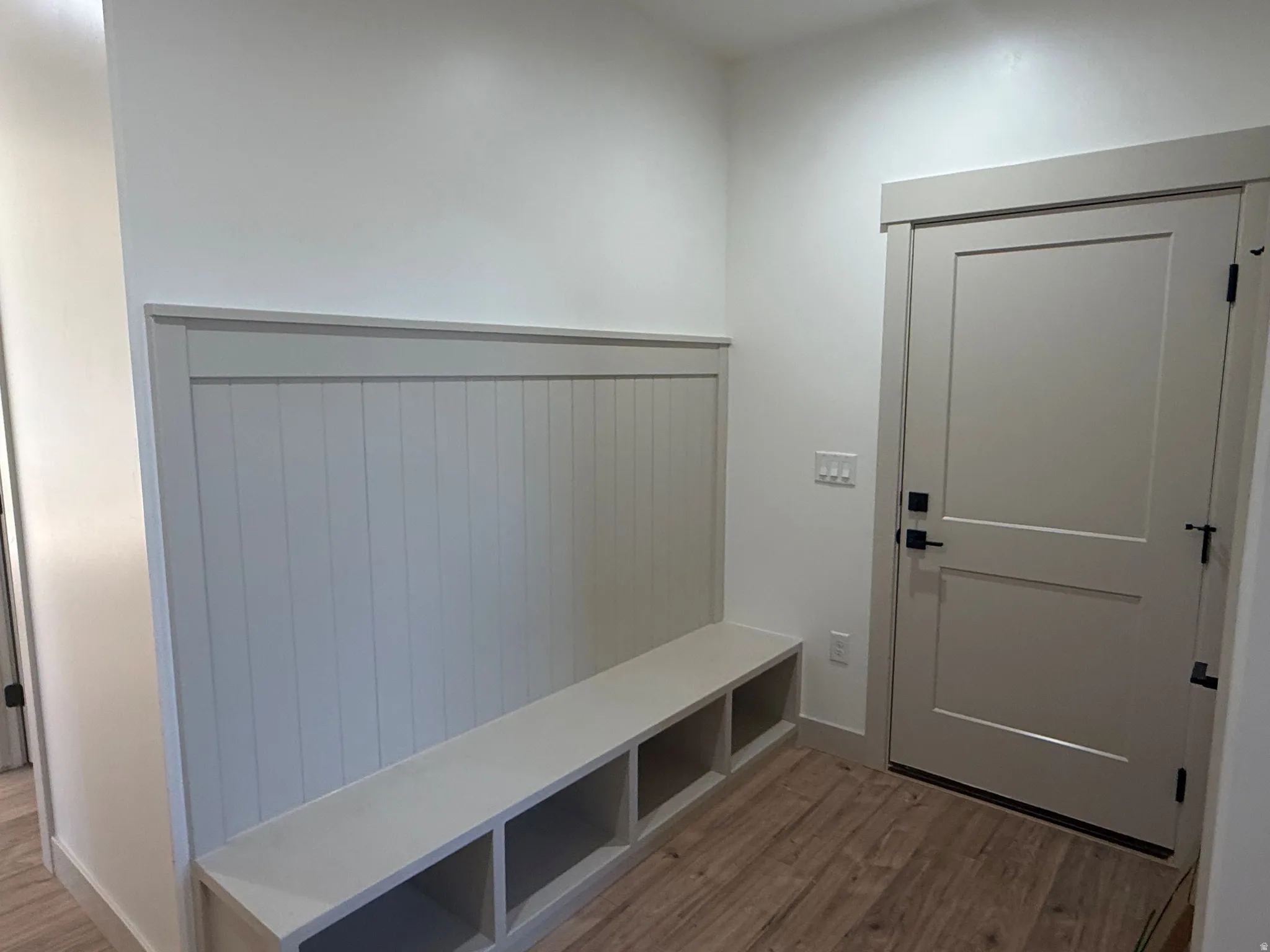 Built-in bench with cubby storage, beadboard wainscoting, and wood-finish flooring