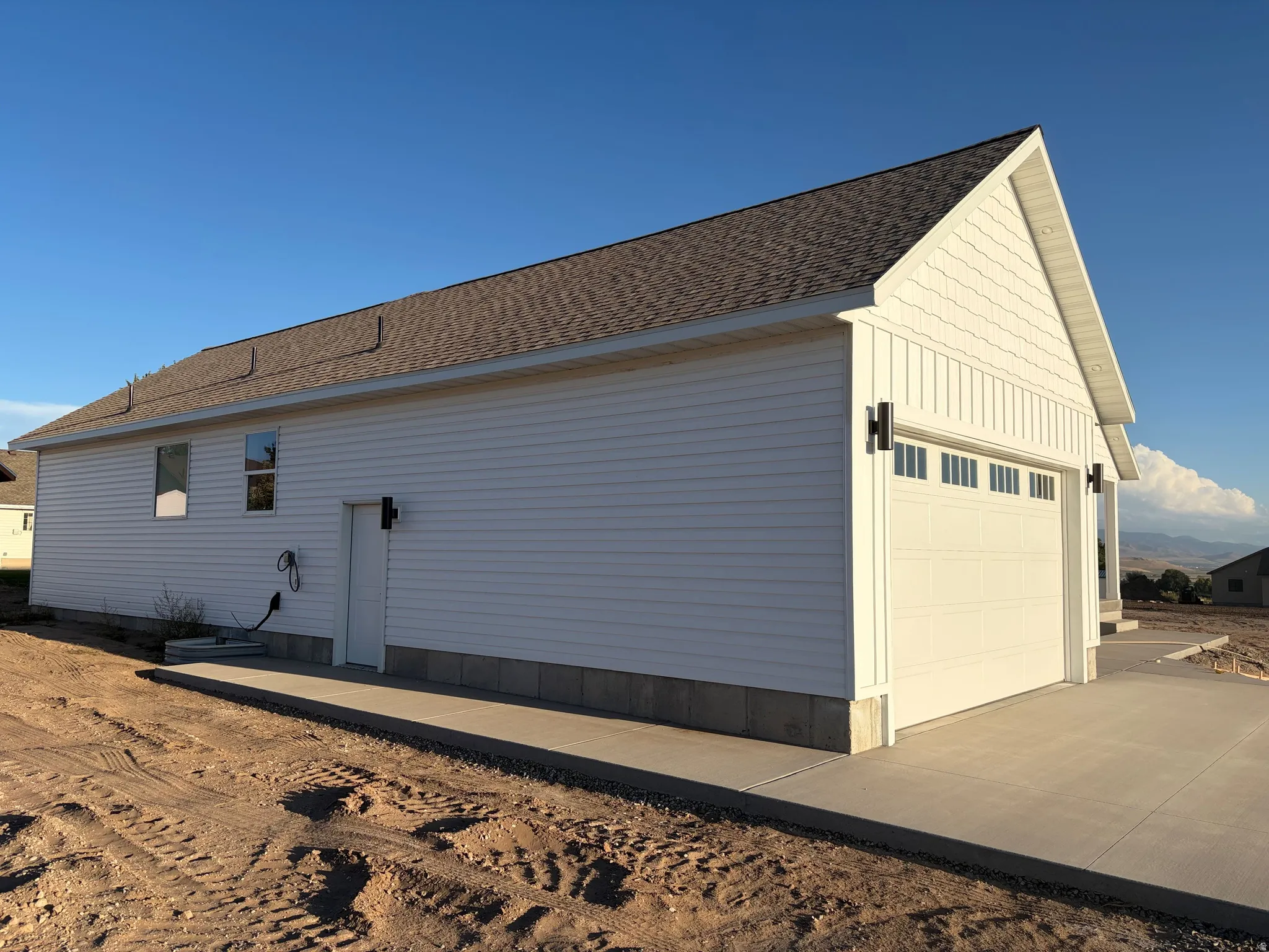 New construction featuring white siding, a prominent garage door with windows, and a paved concrete driveway