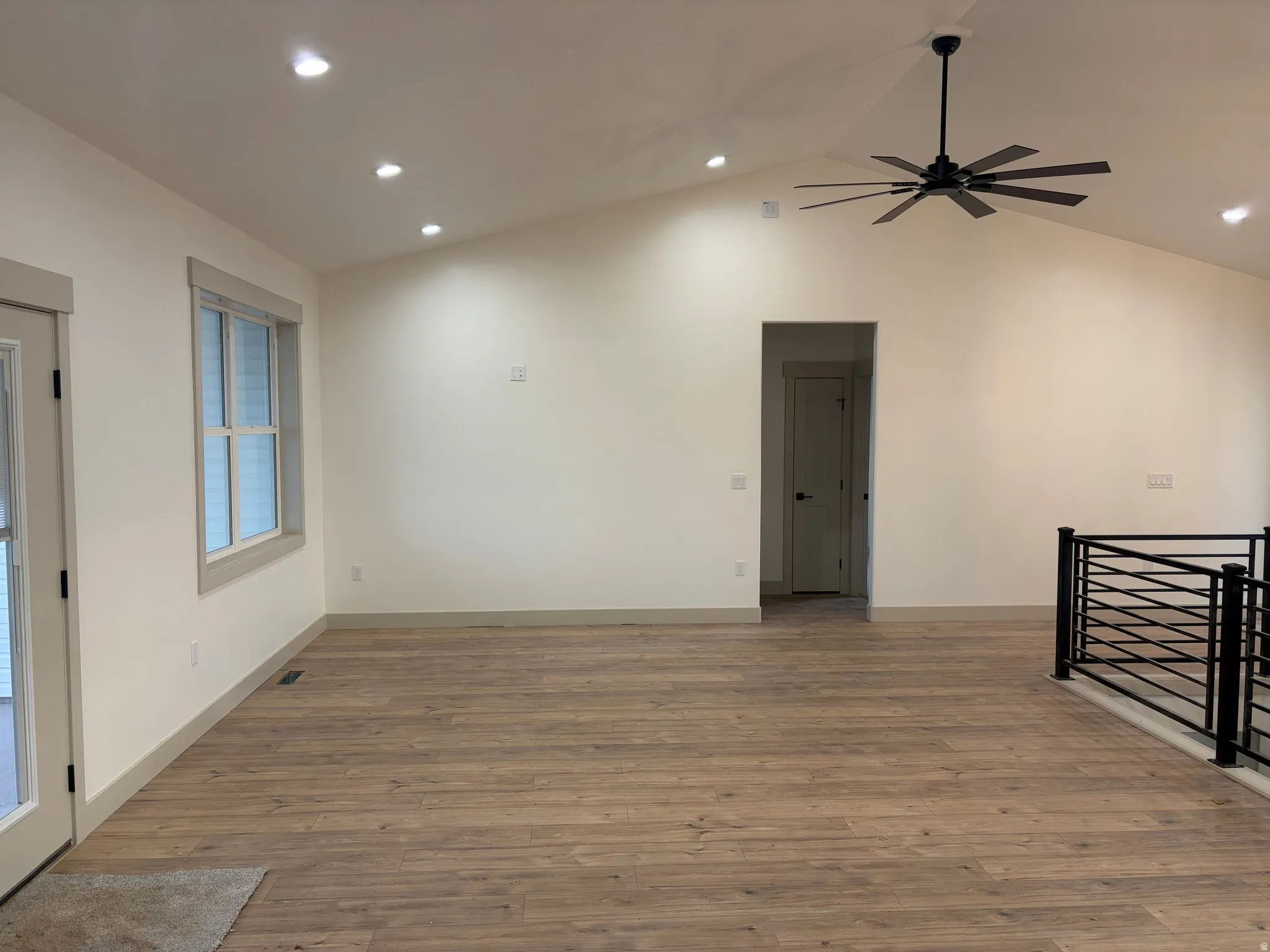 Vaulted ceiling with recessed lighting and a ceiling fan, wood-finish flooring, and a black metal horizontal-bar railing