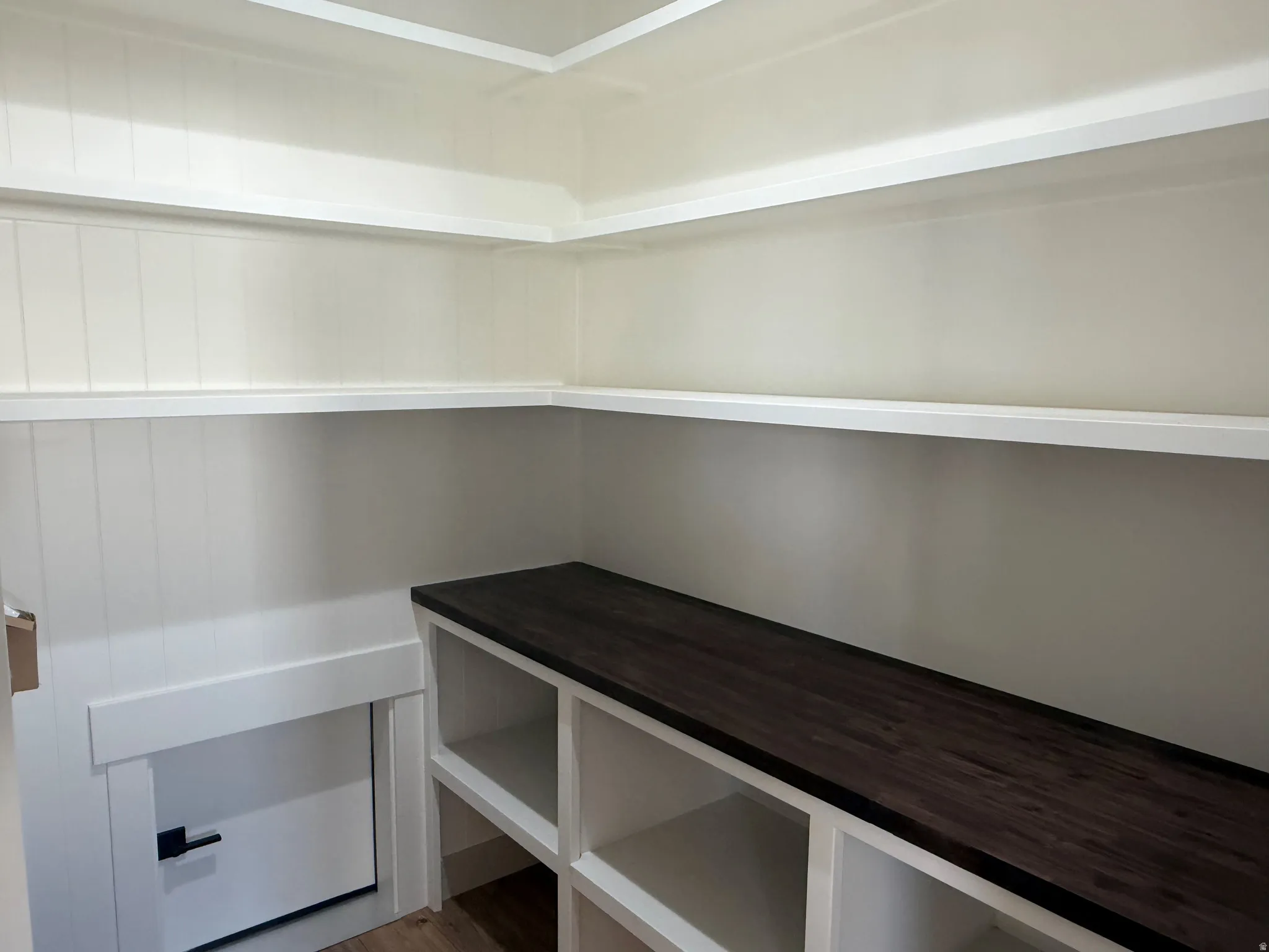Built-in shelving with a dark wood-finish countertop, beadboard wall paneling, and an integrated access door