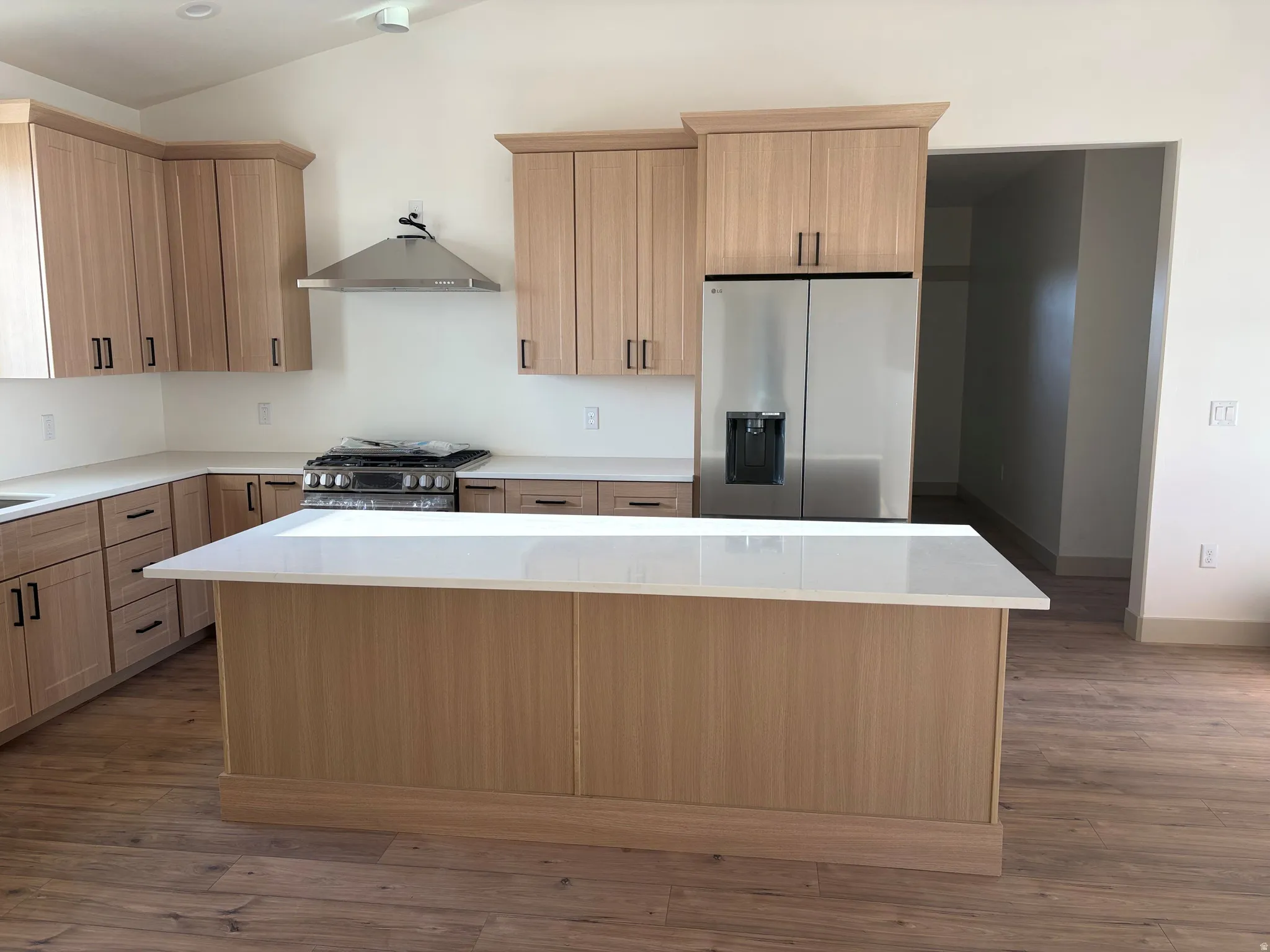 Kitchen featuring light wood-finish cabinetry, stainless steel appliances, a range hood, and a center island with a light-toned countertop