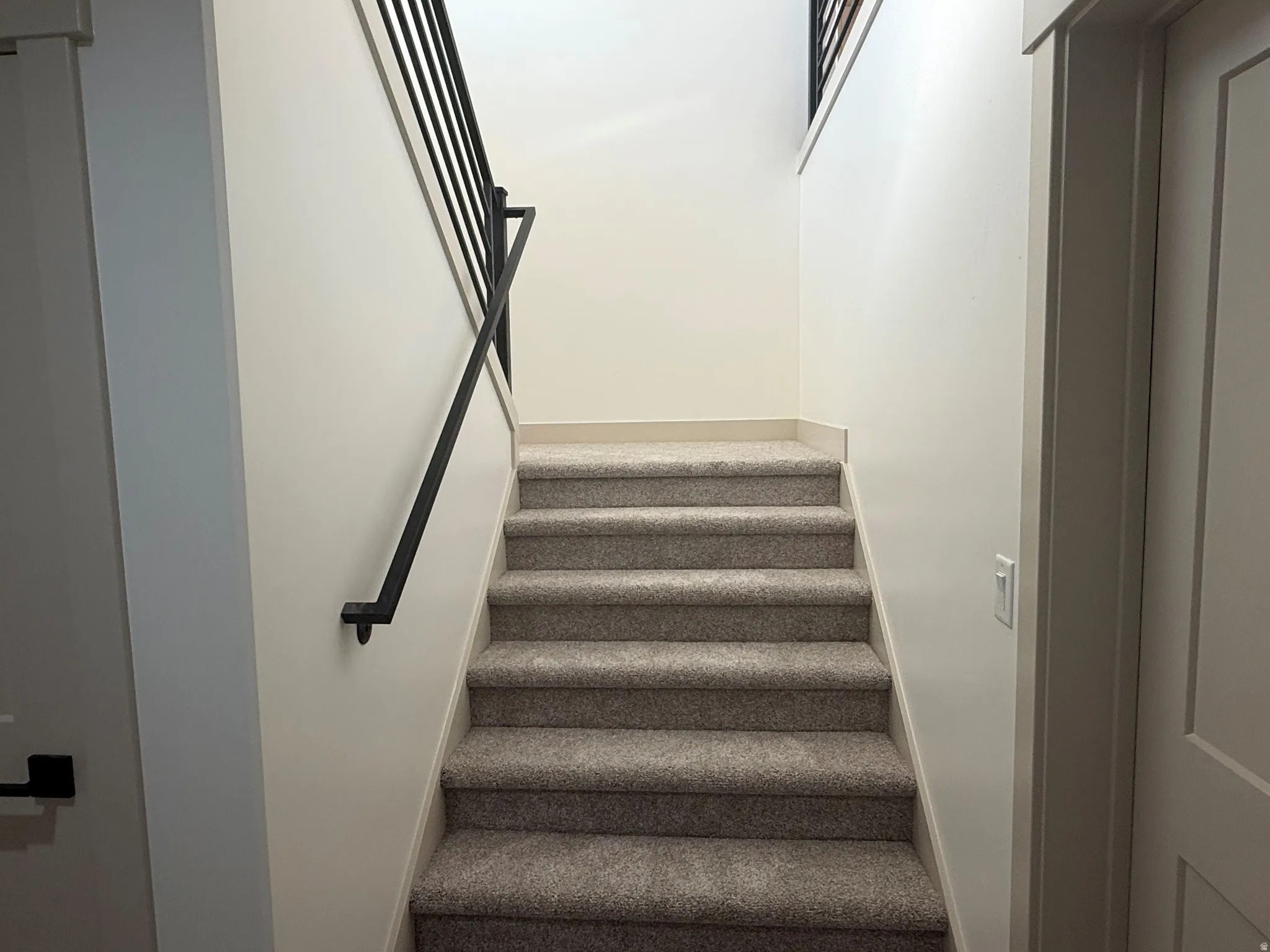 Carpeted staircase featuring a modern black metal handrail and balusters, with a white painted wall and neutral trim