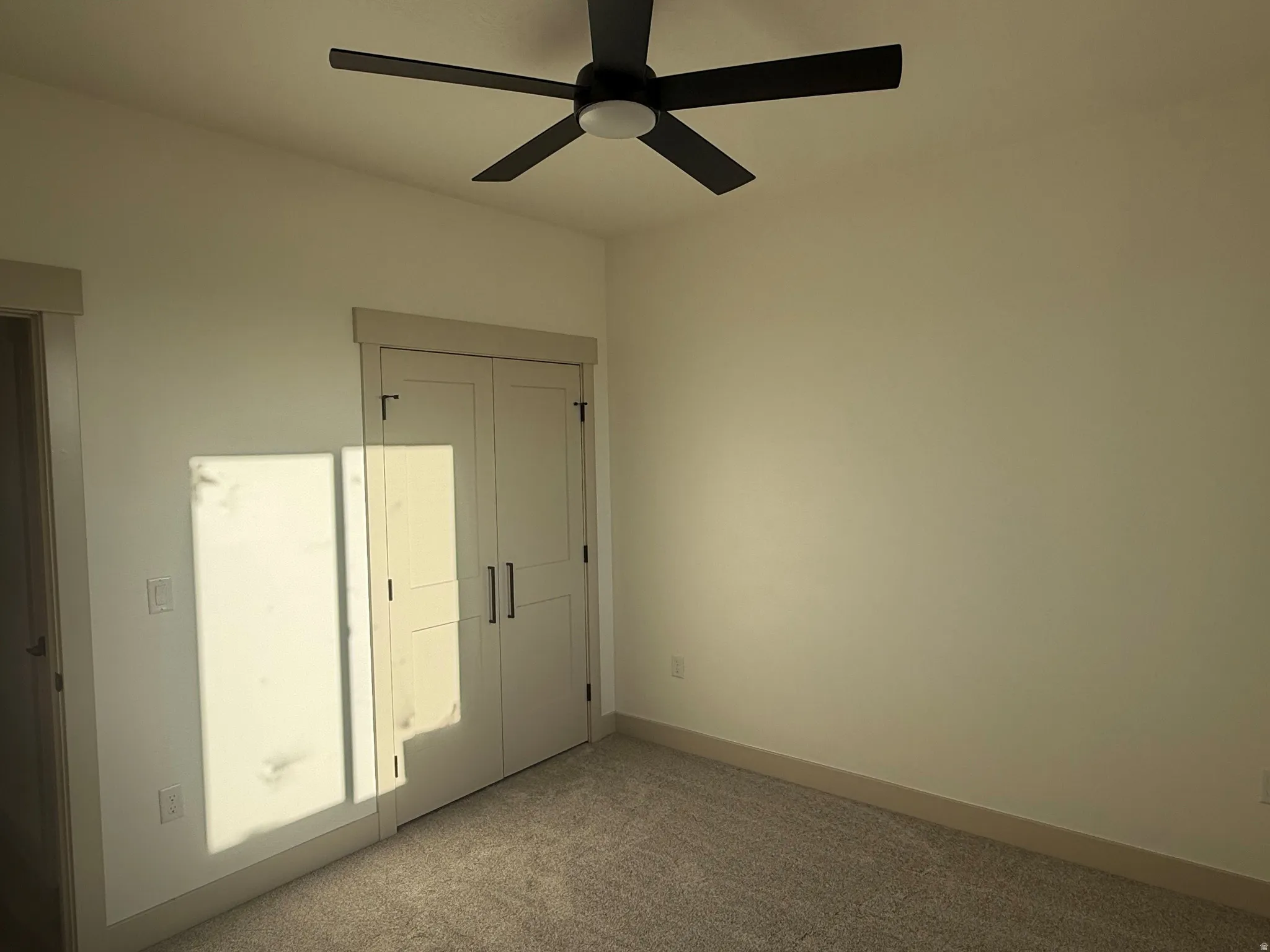 Wall-to-wall carpeting, light-colored walls, ceiling fan with integrated lighting, double closet doors with dark hardware, and wide trim