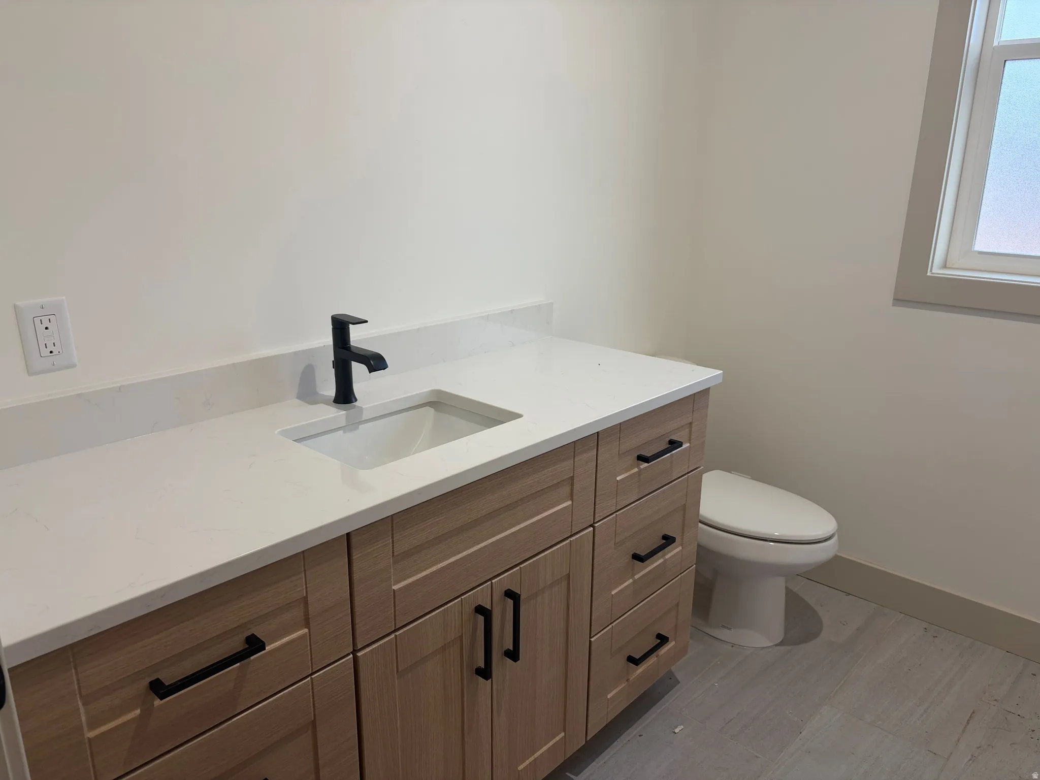 Light wood-finish vanity with ample storage, integrated rectangular sink, matte black faucet, and white countertop