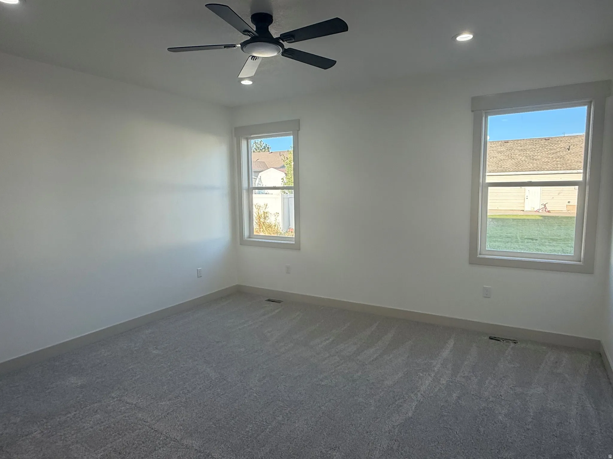 Spacious room featuring neutral carpeting, recessed lighting, ceiling fan, and two windows with white trim