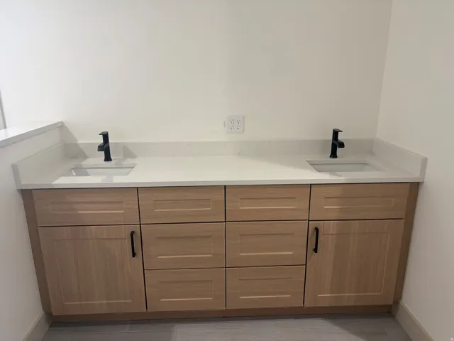 Dual vanity with light wood-finish cabinetry, integrated sinks, black fixtures, and light-toned countertops