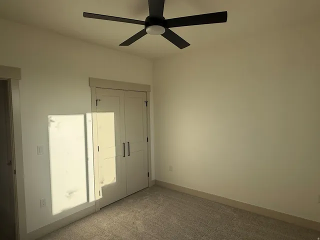 Wall-to-wall carpeting, light-colored walls, ceiling fan with integrated lighting, double closet doors with dark hardware, and wide trim