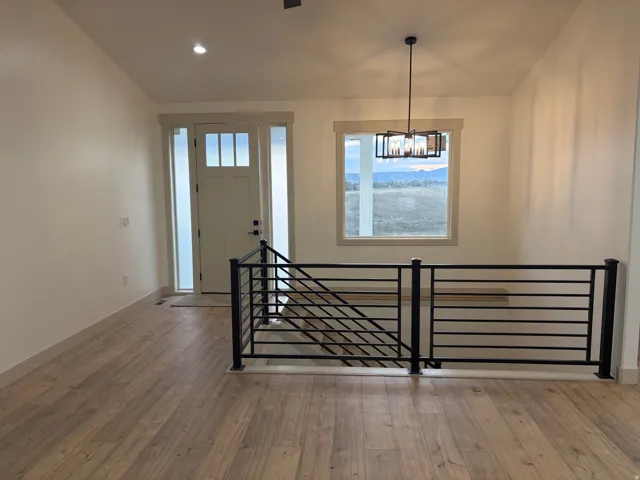 Wood-finish flooring, contemporary black metal railing, prominent window with outdoor scenery, modern entry door with sidelights, and a decorative overhead light fixture
