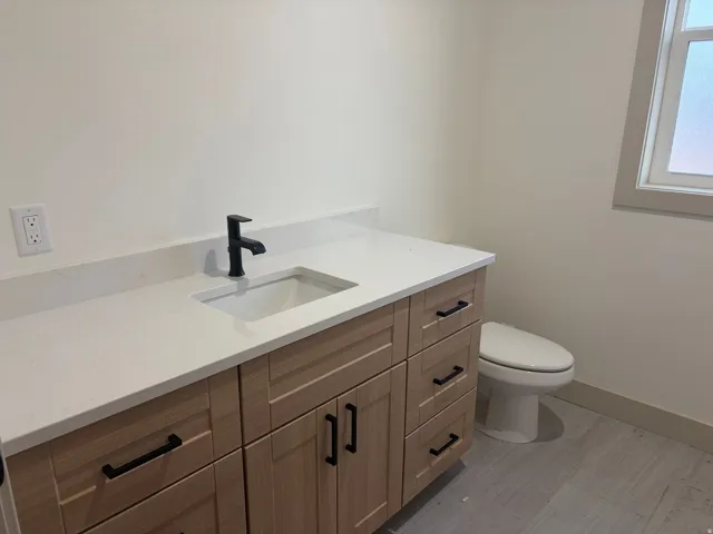Light wood-finish vanity with ample storage, integrated rectangular sink, matte black faucet, and white countertop